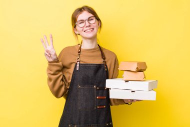 Kızıl saçlı güzel kadın gülümsüyor ve arkadaş canlısı görünüyor, üç numarayı gösteriyor. Fast food yumuşak olsun.