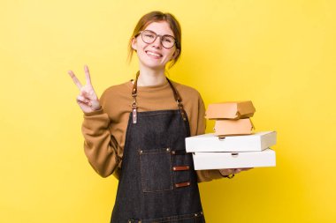 Kızıl saçlı güzel kadın gülümsüyor ve arkadaş canlısı görünüyor, iki numarayı gösteriyor. Fast food yumuşak olsun.