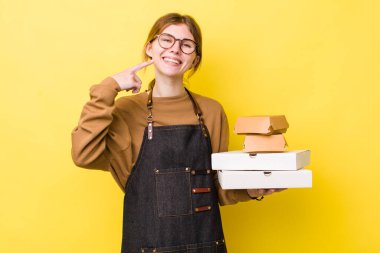 Kızıl saçlı, güzel bir kadın kendi gülüşünü işaret ediyor. Fast food yumuşak olsun.