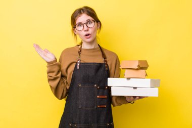 Kızıl saçlı, güzel bir kadın şaşırmış ve şok olmuş görünüyor. Çenesi düşmüş, elinde bir nesne var. Fast food yumuşak olsun.