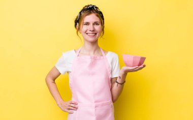 Kızıl saçlı güzel kadın mutlu bir şekilde gülümsüyor, eli kalçasında ve kendinden emin. Ev hanımı elinde boş bir kâse tutuyor.