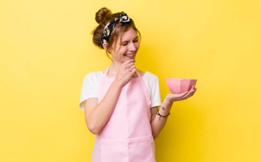 red head pretty woman smiling with a happy, confident expression with hand on chin. housewife holding an empty bowl