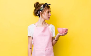 Profil bakışlı kızıl saçlı güzel kadın hayal mi kuruyor yoksa hayal mi kuruyor? Ev hanımı elinde boş bir kâse tutuyor.