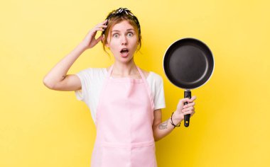 Kızıl saçlı güzel kadın mutlu, şaşkın ve şaşırmış görünüyor. kızartma tavası ve ev hanımı kavramı