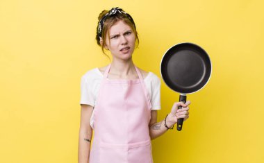 Kızıl saçlı güzel kadın şaşkın ve şaşkın hissediyor. kızartma tavası ve ev hanımı kavramı