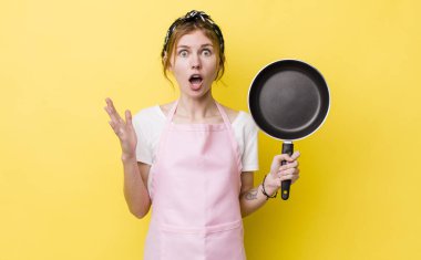 red head pretty woman feeling extremely shocked and surprised. fry pan and housewife concept