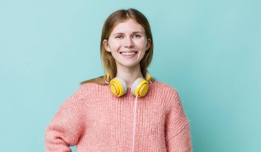Kızıl saçlı güzel kadın mutlu bir şekilde gülümsüyor, eli kalçasında ve kendinden emin. kulaklıklar ve müzik konsepti