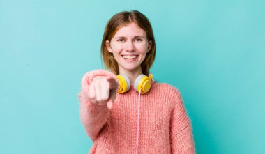 Kızıl saçlı güzel kadın kamerayı işaret ederek seni seçiyor. kulaklıklar ve müzik konsepti