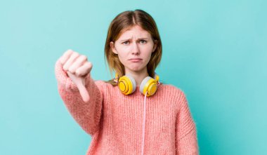 Kızıl saçlı, güzel bir kadın kendini kötü hissediyor, baş parmağını kaldırıyor. kulaklıklar ve müzik konsepti