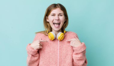 Kızıl saçlı güzel bir kadın mutlu hissediyor ve heyecanla kendini işaret ediyor. kulaklıklar ve müzik konsepti