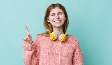 Kızıl saçlı güzel kadın gülümsüyor ve arkadaş canlısı görünüyor, bir numarayı gösteriyor. kulaklıklar ve müzik konsepti