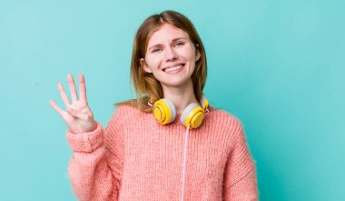 Kızıl saçlı güzel kadın gülümsüyor ve arkadaş canlısı görünüyor, dört numarayı gösteriyor. kulaklıklar ve müzik konsepti