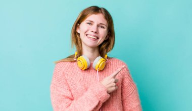 Kızıl saçlı güzel bir kadın neşeyle gülümsüyor, mutlu hissediyor ve bir tarafı işaret ediyor. kulaklıklar ve müzik konsepti