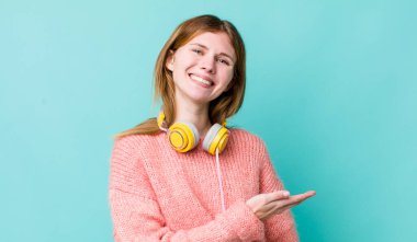 kızıl saçlı güzel bir kadın neşeli bir şekilde gülümsüyor, mutlu hissediyor ve bir konsept gösteriyor. kulaklıklar ve müzik konsepti