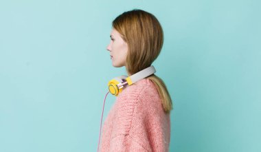 red head pretty woman on profile view thinking, imagining or daydreaming. headphones and music concept