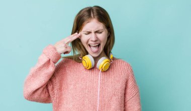 Kızıl saçlı güzel bir kadın mutsuz ve stresli görünüyor, intihar jesti silah işareti yapıyor. kulaklıklar ve müzik konsepti