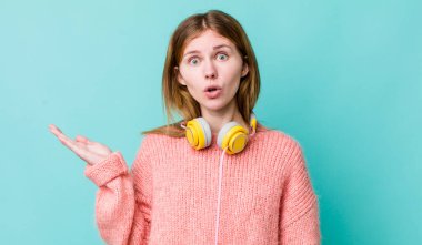 Kızıl saçlı, güzel bir kadın şaşırmış ve şok olmuş görünüyor. Çenesi düşmüş, elinde bir nesne var. kulaklıklar ve müzik konsepti