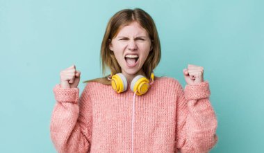 Kızıl saçlı güzel bir kadın sinirli bir ifadeyle agresif bir şekilde bağırıyor. kulaklıklar ve müzik konsepti