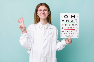 Kızıl saçlı güzel kadın gülümsüyor ve arkadaş canlısı görünüyor, üç numarayı gösteriyor. optik görüş testi konsepti