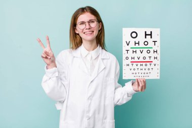 Kızıl saçlı güzel kadın gülümsüyor ve arkadaş canlısı görünüyor, iki numarayı gösteriyor. optik görüş testi konsepti