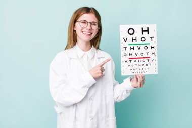 Kızıl saçlı güzel bir kadın neşeyle gülümsüyor, mutlu hissediyor ve bir tarafı işaret ediyor. optik görüş testi konsepti