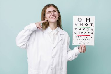 Kızıl saçlı, güzel bir kadın kendi gülüşünü işaret ediyor. optik görüş testi konsepti