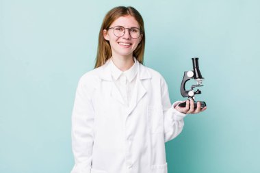 Kızıl saçlı güzel kadın mutlu bir şekilde gülümsüyor, eli kalçasında ve kendinden emin. Mikroskop konseptine sahip bilim adamı