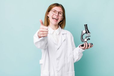 Kızıl saçlı güzel bir kadın gururlu, olumlu gülümsüyor. Mikroskop konseptine sahip bilim adamı