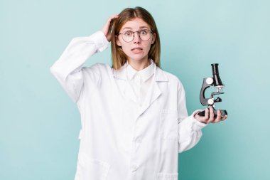 Kızıl saçlı güzel kadın stresli, endişeli ya da korkmuş, elleri başının üstünde. Mikroskop konseptine sahip bilim adamı