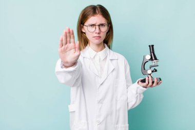 Kızıl saçlı güzel kadın ciddi görünüyor. Avuç içini gösteriyor. Durdurma hareketi yapıyor. Mikroskop konseptine sahip bilim adamı