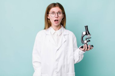 Kızıl saçlı güzel kadın çok şaşırmış ya da şaşkın görünüyor. Mikroskop konseptine sahip bilim adamı