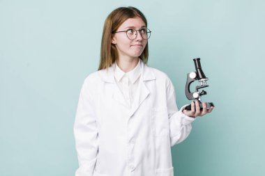 Kızıl saçlı güzel kadın omuz silkiyor, kafası karışık ve kararsız. Mikroskop konseptine sahip bilim adamı