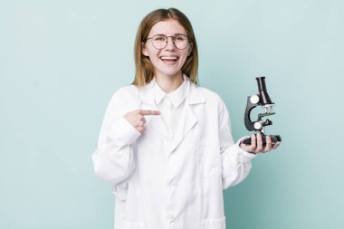Kızıl saçlı güzel bir kadın mutlu hissediyor ve heyecanla kendini işaret ediyor. Mikroskop konseptine sahip bilim adamı