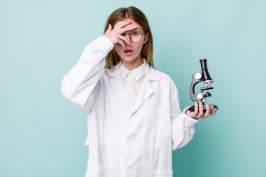 Kızıl saçlı güzel bir kadın şok olmuş, korkmuş ya da korkmuş görünüyor. Mikroskop konseptine sahip bilim adamı