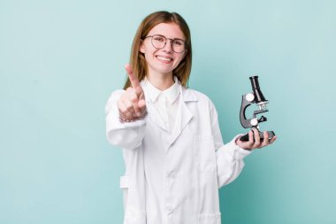 Kızıl saçlı güzel kadın gururla gülümsüyor ve kendinden emin bir numara oluyor. Mikroskop konseptine sahip bilim adamı