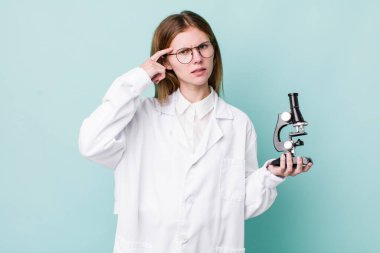 Kızıl saçlı güzel kadın kafası karışık ve şaşkın hissediyor, deli olduğunu gösteriyor. Mikroskop konseptine sahip bilim adamı