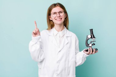 Kızıl saçlı güzel kadın gülümsüyor ve arkadaş canlısı görünüyor, bir numarayı gösteriyor. Mikroskop konseptine sahip bilim adamı