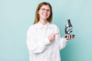 Kızıl saçlı güzel bir kadın neşeyle gülümsüyor, mutlu hissediyor ve bir tarafı işaret ediyor. Mikroskop konseptine sahip bilim adamı