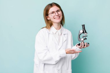 kızıl saçlı güzel bir kadın neşeli bir şekilde gülümsüyor, mutlu hissediyor ve bir konsept gösteriyor. Mikroskop konseptine sahip bilim adamı