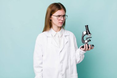 Kızıl saçlı, güzel bir kadın üzgün, üzgün ya da kızgın ve yana bakıyor. Mikroskop konseptine sahip bilim adamı