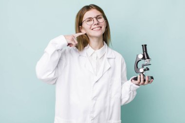 Kızıl saçlı, güzel bir kadın kendi gülüşünü işaret ediyor. Mikroskop konseptine sahip bilim adamı