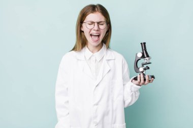 Kızıl saçlı, güzel bir kadın agresif bir şekilde bağırıyor, çok kızgın görünüyor. Mikroskop konseptine sahip bilim adamı