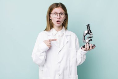 Kızıl saçlı güzel kadın şok olmuş ve ağzı açık, kendini işaret eden bir şekilde şaşırmış görünüyor. Mikroskop konseptine sahip bilim adamı