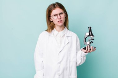 Kızıl saçlı güzel kadın şaşkın ve şaşkın hissediyor. Mikroskop konseptine sahip bilim adamı