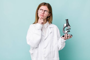 Kızıl saçlı güzel kadın düşünüyor, kuşkulu ve şaşkın hissediyor. Mikroskop konseptine sahip bilim adamı