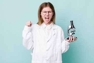 red head pretty woman shouting aggressively with an angry expression. scientist with microscope concept