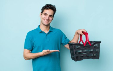 Yakışıklı İspanyol adam neşeyle gülümsüyor, mutlu hissediyor ve bir konsept gösteriyor. Alışveriş sepeti konsepti
