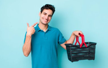 Yakışıklı İspanyol adam kendine güvenerek gülümsedi ve kendi gülüşünü gösterdi. Alışveriş sepeti konsepti