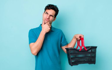 Yakışıklı İspanyol adam düşünüyor, kuşkulu ve şaşkın hissediyor. Alışveriş sepeti konsepti