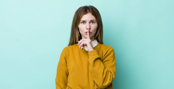 Красная голова красивая женщина выглядит серьезным и крест с пальцем прижаты к губам требуя тишины или тишины, сохраняя секрет